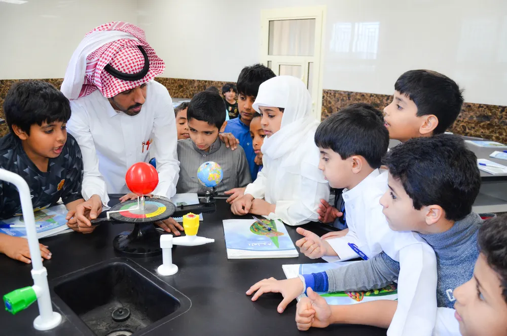 Saudi teacher demonstrating a solar system model to a group of young students in a classroom.