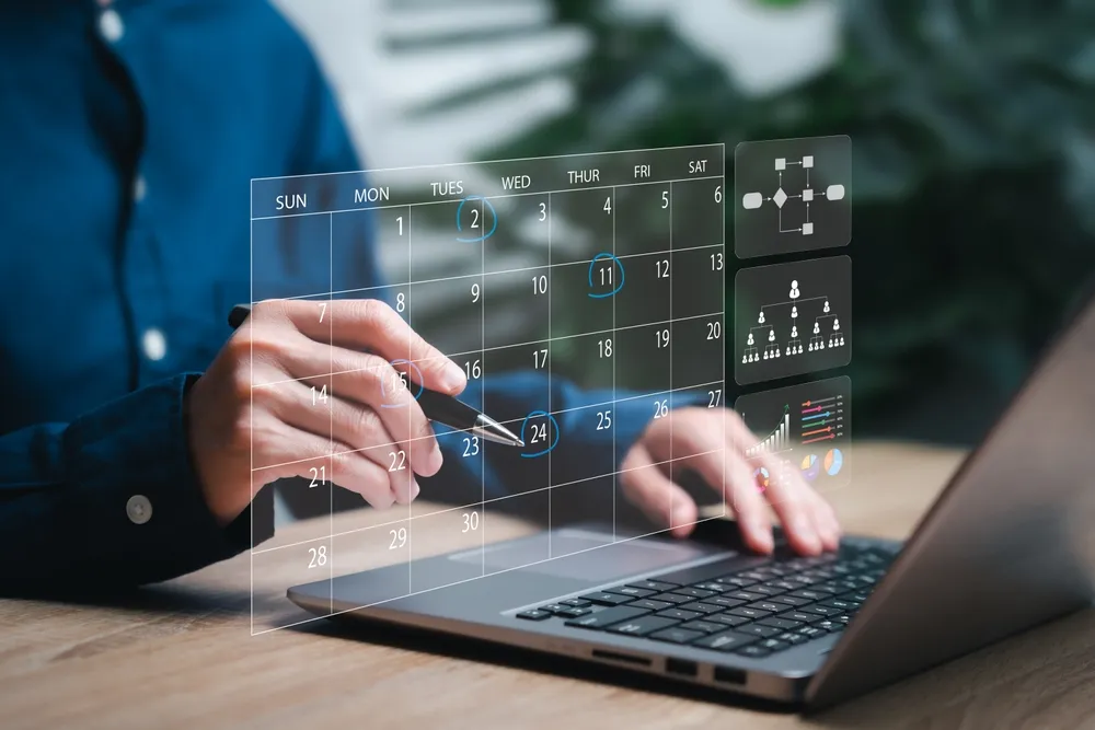 Professional using a laptop with a holographic calendar and data analytics for event management.