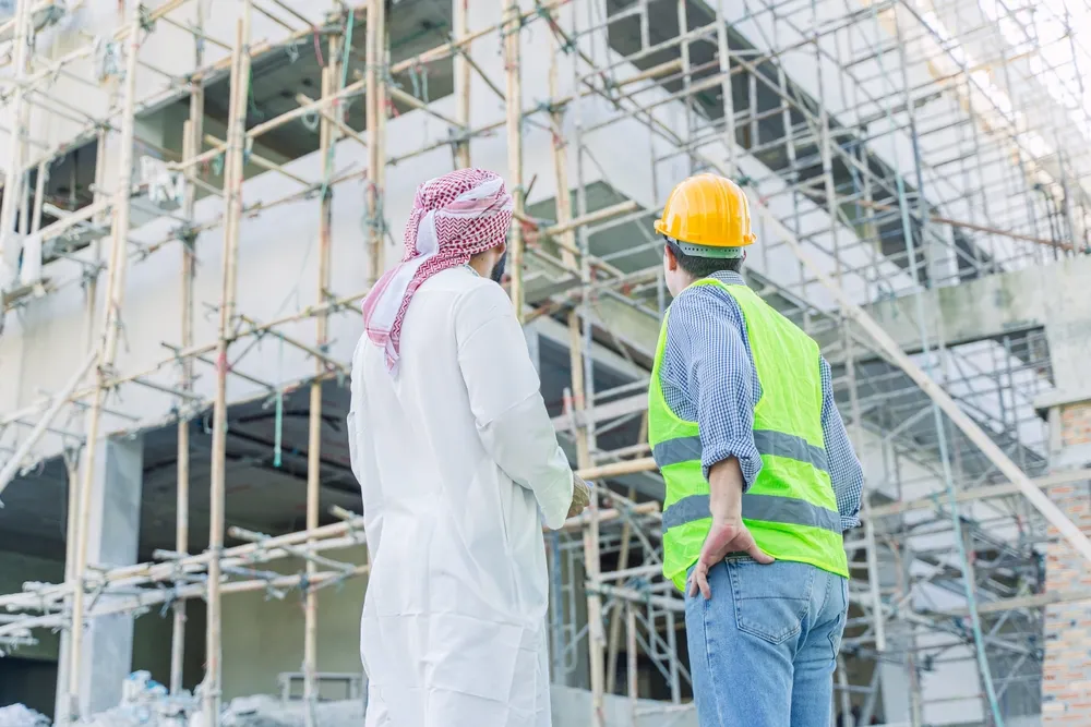 Two professionals observing a construction site with scaffolding in Saudi Arabia's real estate