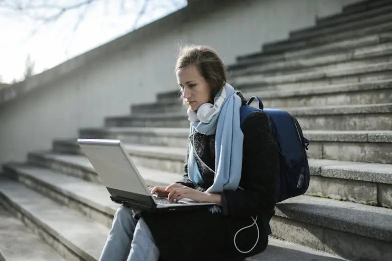 student-sitting-on-stairs-outside-using-laptop